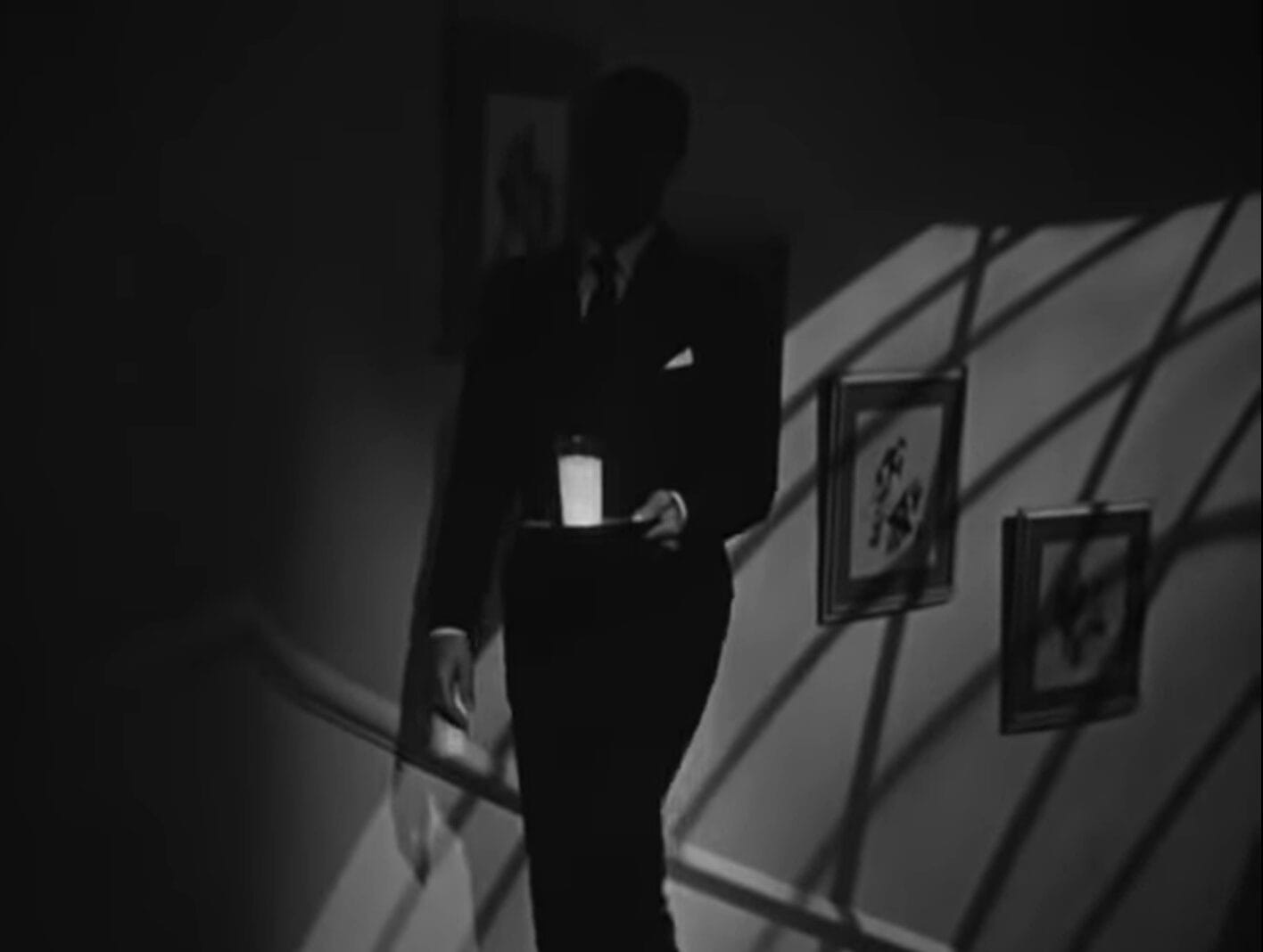 un hombre sube con un vaso de leche que contiene veneno, de una escena de una película de suspenso de Alfred Hitchcock